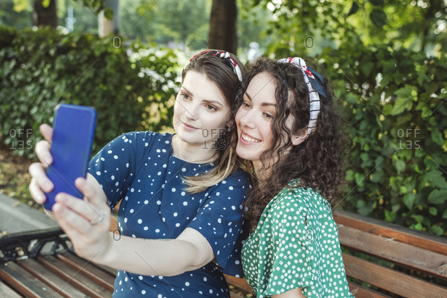 Beautiful woman taking selfie with young female friend sitting at park