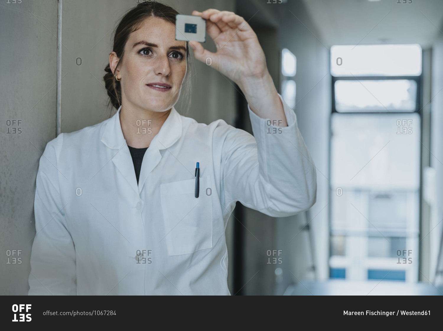 Female scientist holding computer chip while leaning on wall at clinic