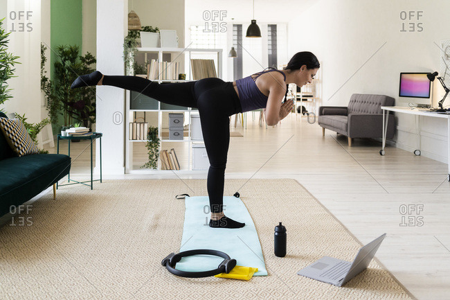 Young female athlete with one leg up standing on exercise mat at home
