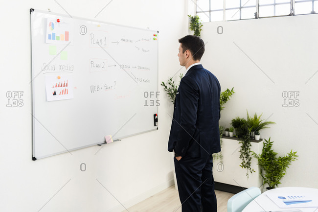 Young male entrepreneur looking at strategy on whiteboard in office