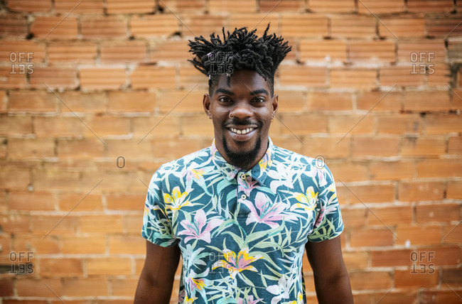 Smiling mid adult man with locs standing against brick wall in city