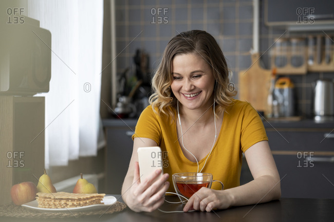 Happy woman having a video chat with smartphone in kitchen at home