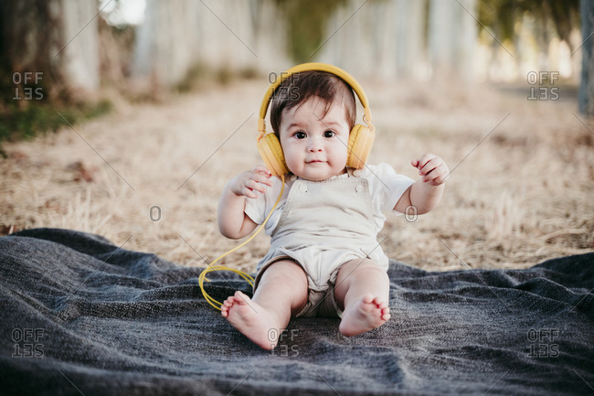 Cute baby boy wearing headphones while sitting on blanket outdoors