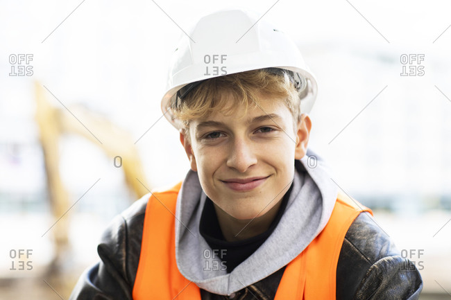 Smiling male teenage construction trainee wearing hardhat at site