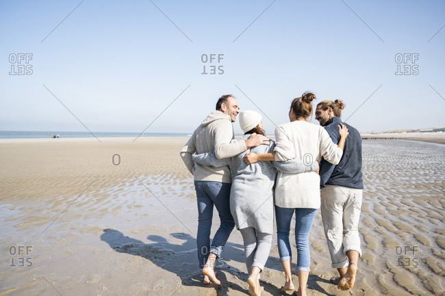Family with arms around talking while walking together at beach