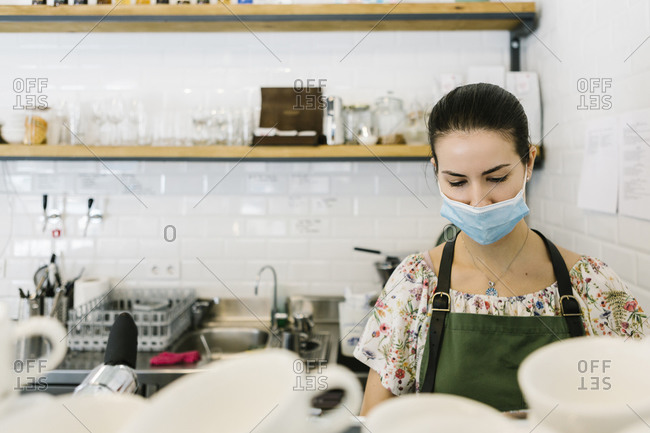 Woman wearing face mask while working in kitchen at coffee shop