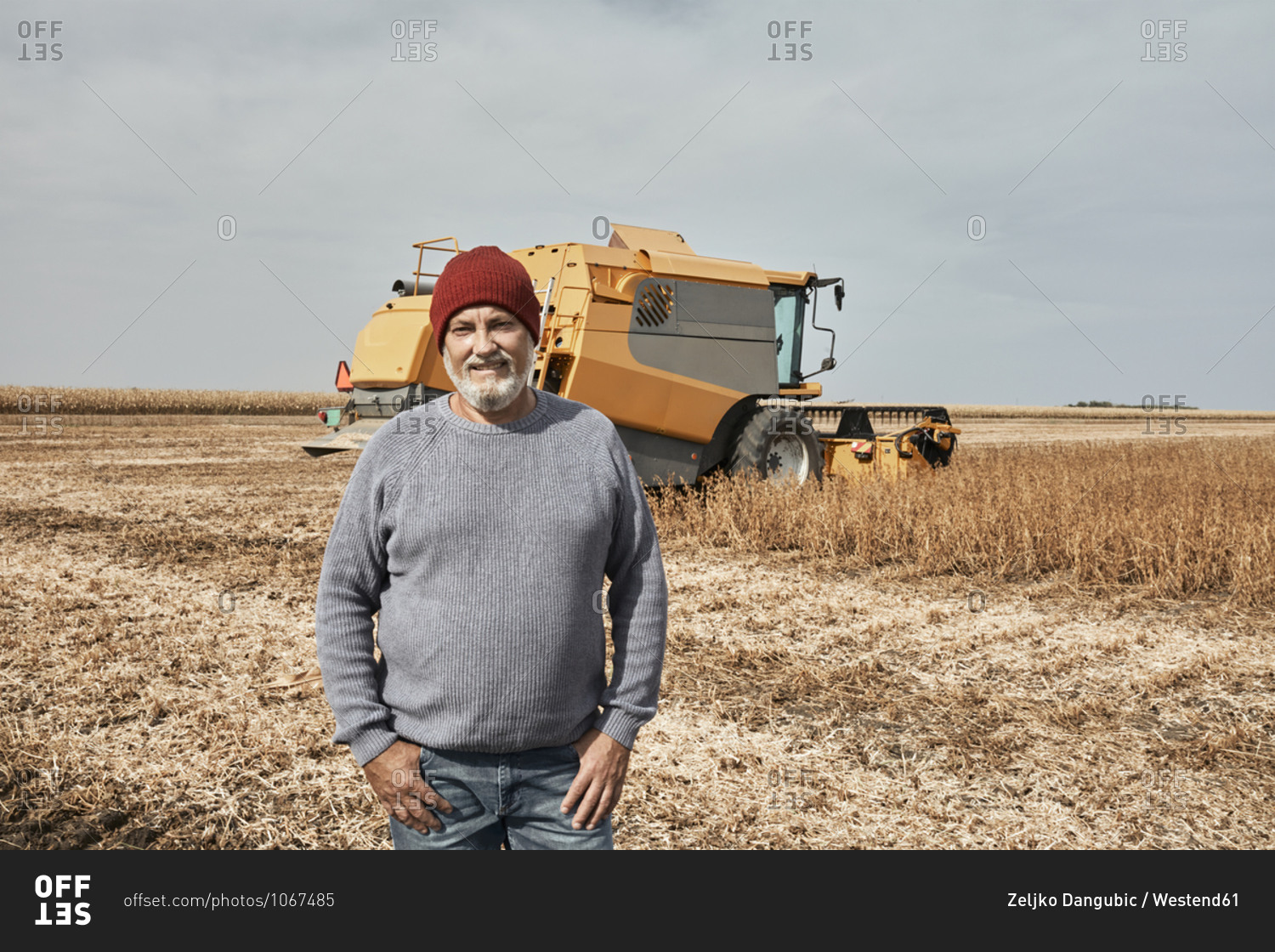 Smiling farmer standing against tractor harvesting crop at farm
