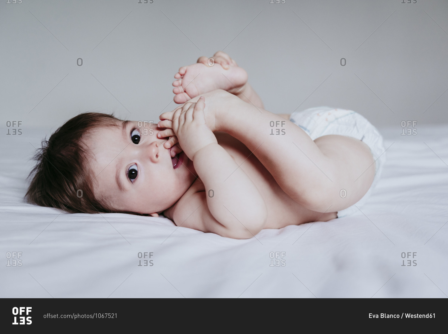 Cute baby boy putting foot in mouth while lying on bed at home