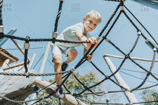 Boy climbing on spider web in public park during sunny day