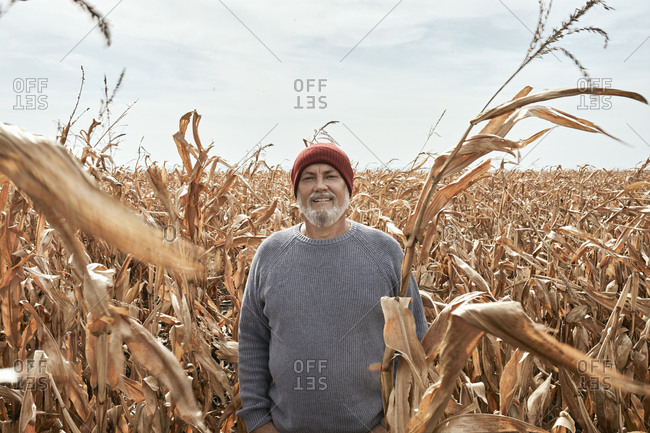 Smiling farmer standing at corn field during sunny day