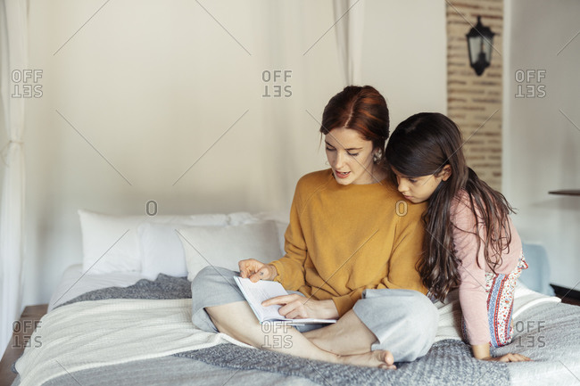 Mother teaching daughter while sitting on bed at home