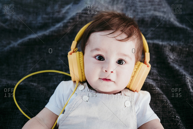 Baby boy wearing headphones lying on blanket outdoors