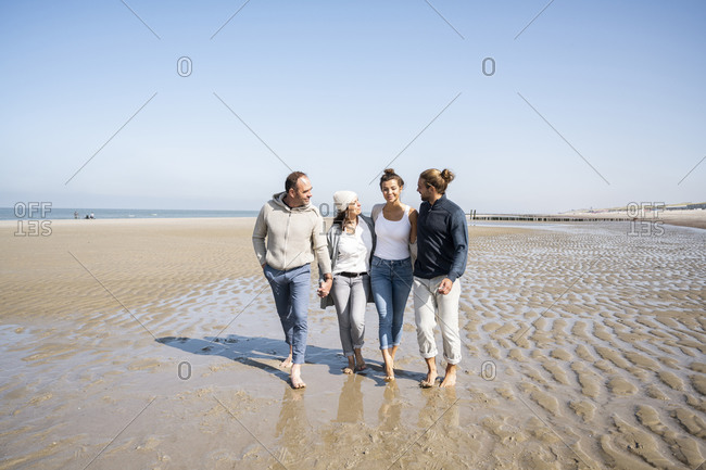 Smiling couples walking with arm around at beach