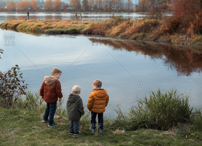 Three little boys looking out at pond in autumn