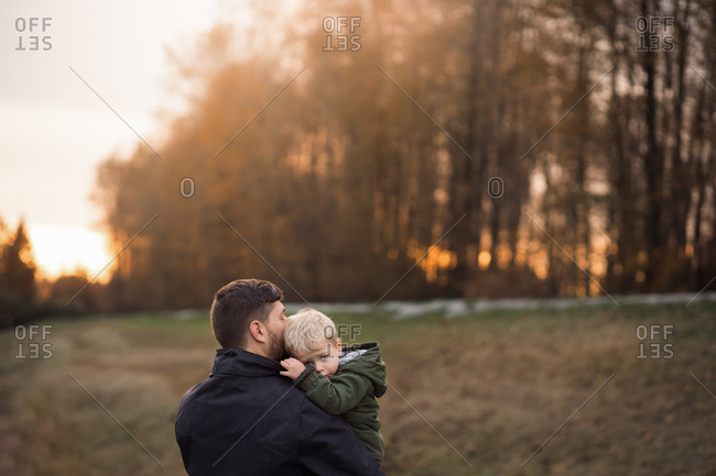 Father carrying his toddler son while walking together at sunset