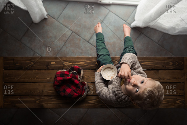 Overhead view of toddler boy sitting on a wooden bench drinking cocoa