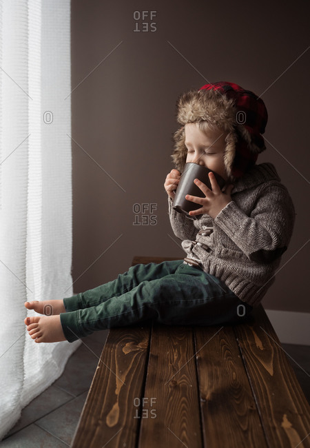 Toddler boy sitting on a wooden bench drinking cocoa