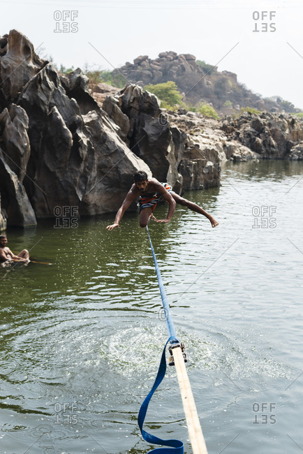 Hampi, Karnataka, India - April 09, 2019: Front view of acrobatic Indian male doing tightrope balancing above the waters of a river