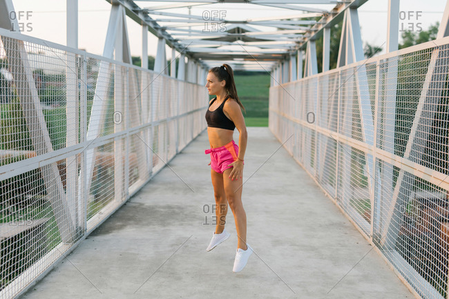 Young adult female runner warming up by doing jumps before a workout on a pedestrian bridge