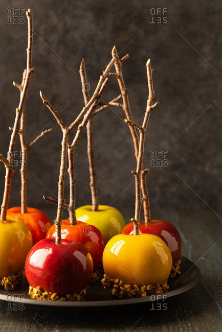 Green and red caramel apples with branch sticks on a black plate