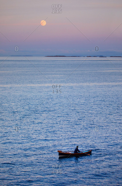 Man rowing a wooden boat at dusk with moon rising in distance near Sidney, British Columbia, Canada