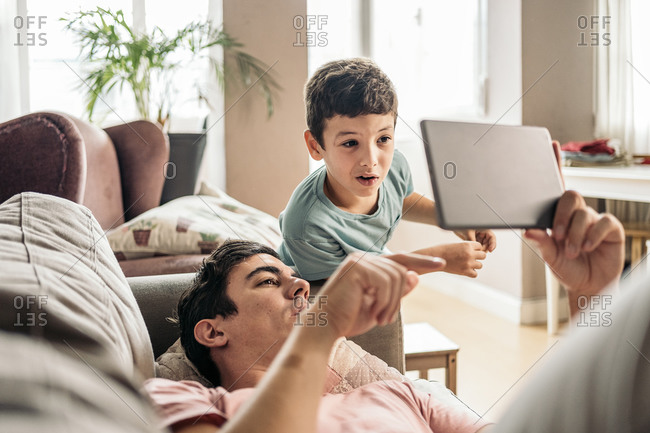 Happy father having fun with his young son using tablet at home in Spain
