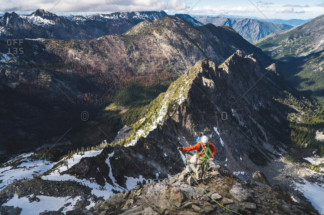 Man coiling rope on rock climb with tall mountains behind