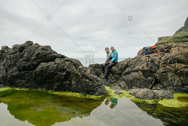 Couple sitting on stones near calm sea water