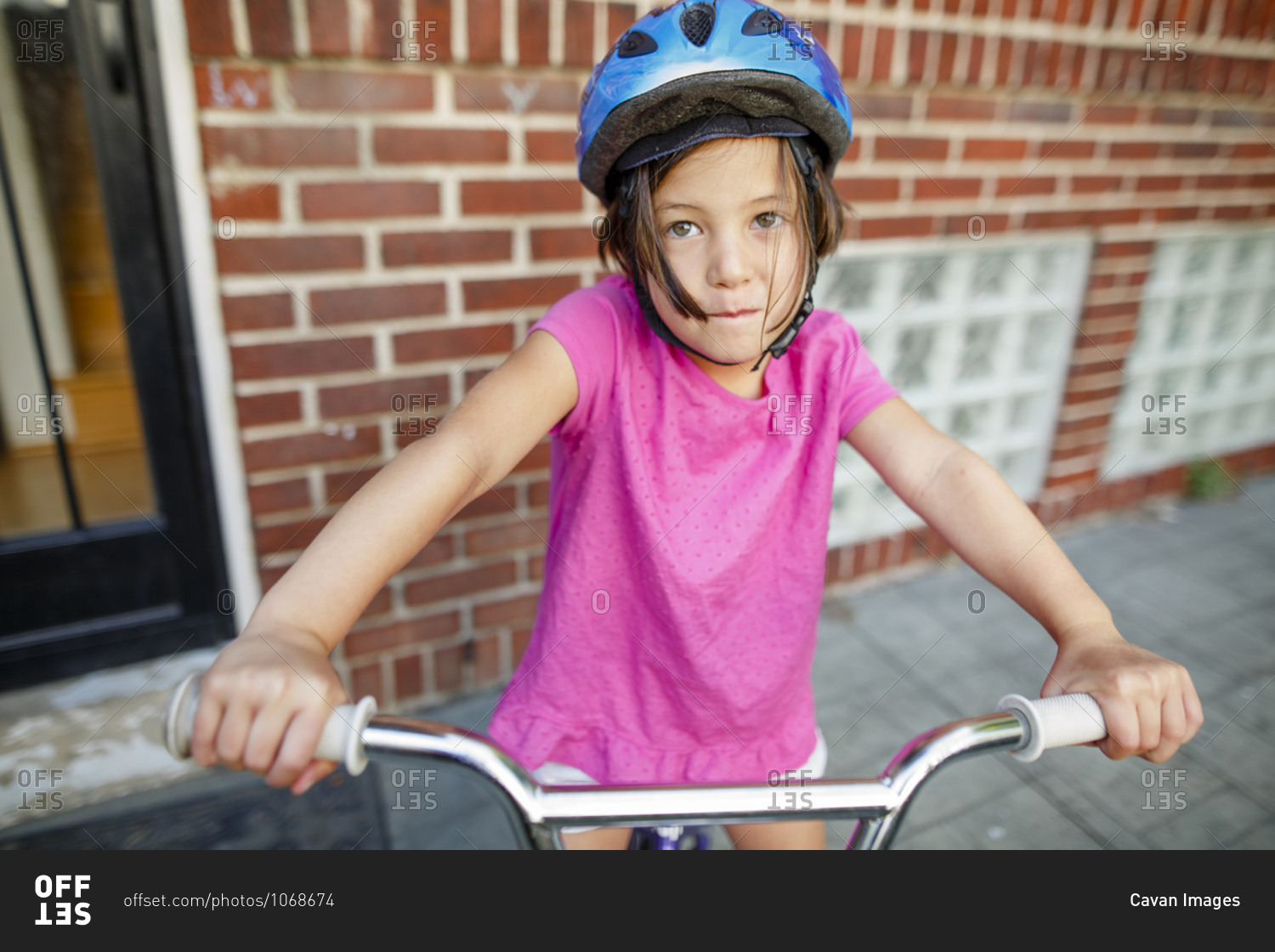 A cute little girl sits on her bike in front of house wearing a helmet