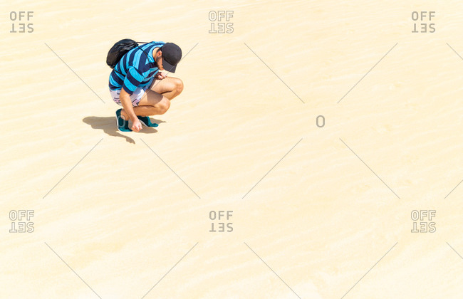 Young man crouching in the dunes of a desert on a sunny and hot day.