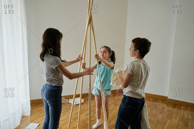 Children putting the sticks to build a teepee tent inside their house.