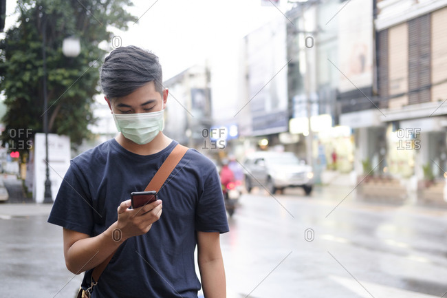 Young man with protective face mask using mobile phone in city