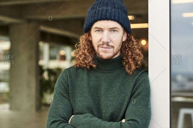 Handsome male hipster wearing knit hat while leaning on window at studio apartment