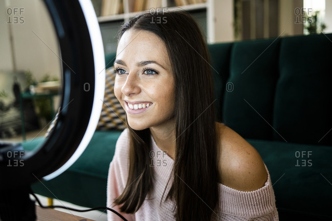 Smiling beautiful female vlogger with illuminated lighting equipment at home