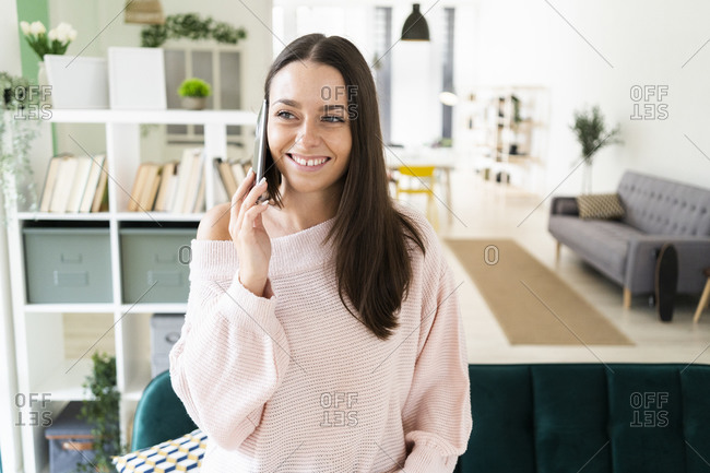 Smiling beautiful woman talking on mobile phone while standing in living room at loft apartment