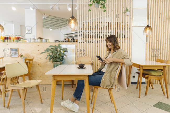 Smiling businesswoman text messaging on smart phone while sitting in cafe