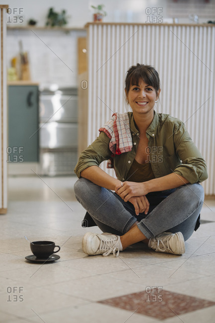 Smiling female owner with cross legged sitting on floor in cafe