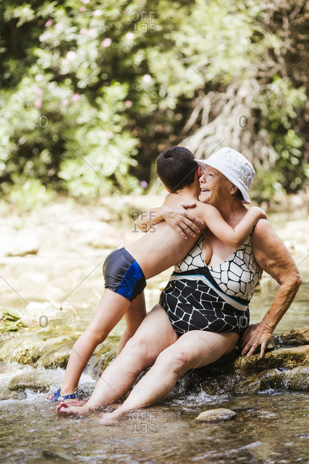 Grandson embracing grandson while sitting on stone in river at forest