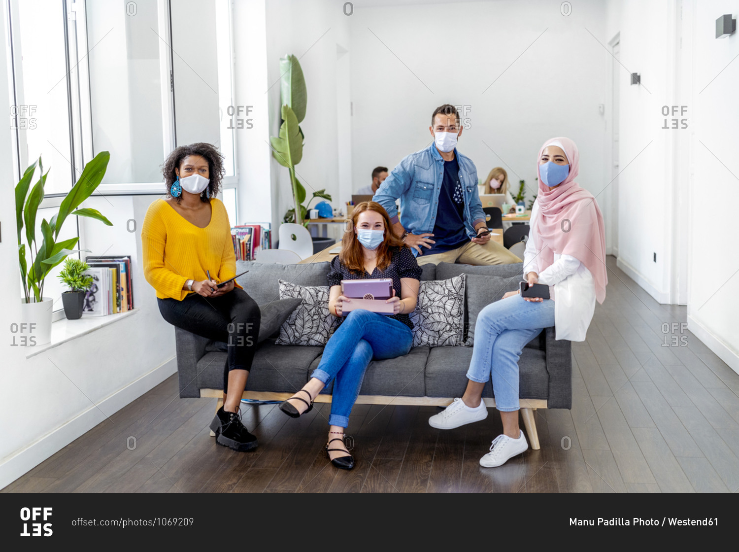 Employees wearing face mask maintaining social distance while sitting with coworker in background at office during COVID-19