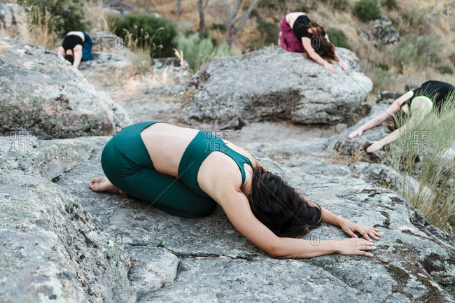 Flexible female friends practicing yoga on rocks