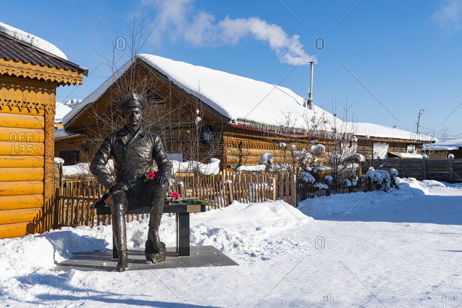 March 3, 2020: Russia- Republic of Sakha- Yakutsk- Statue of soldier sitting on bench in front of rustic houses in winter