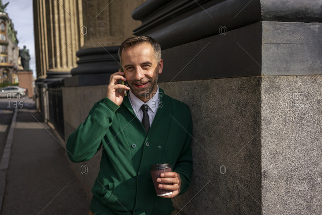 Smiling businessman talking on mobile phone while leaning on pillar of Kazan Cathedral at Saint Petersburg- Russia