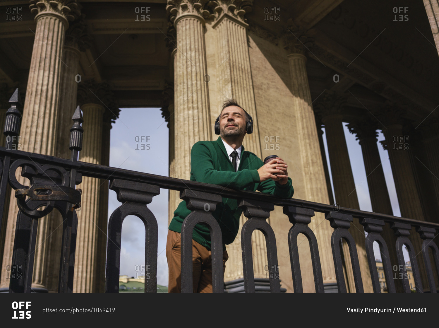 Businessman with headphones holding coffee cup leaning on railing at Kazan Cathedral at Saint Petersburg- Russia