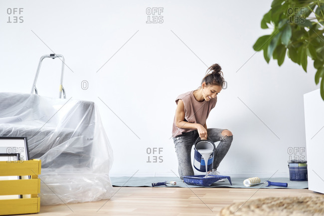 Smiling young woman pouring paint in paint tray while kneeling at home