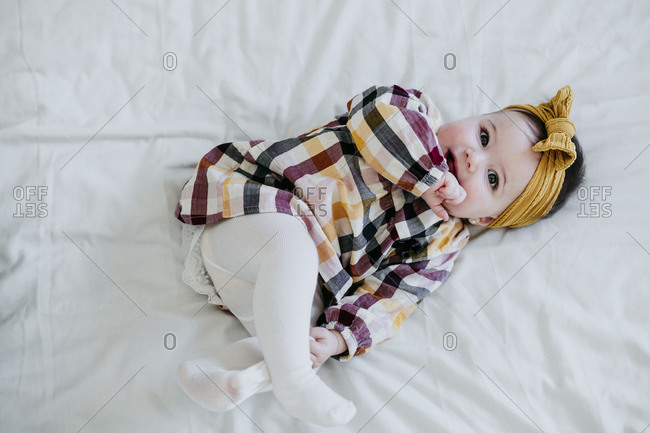 Cute baby girl with finger in mouth lying on bed at home