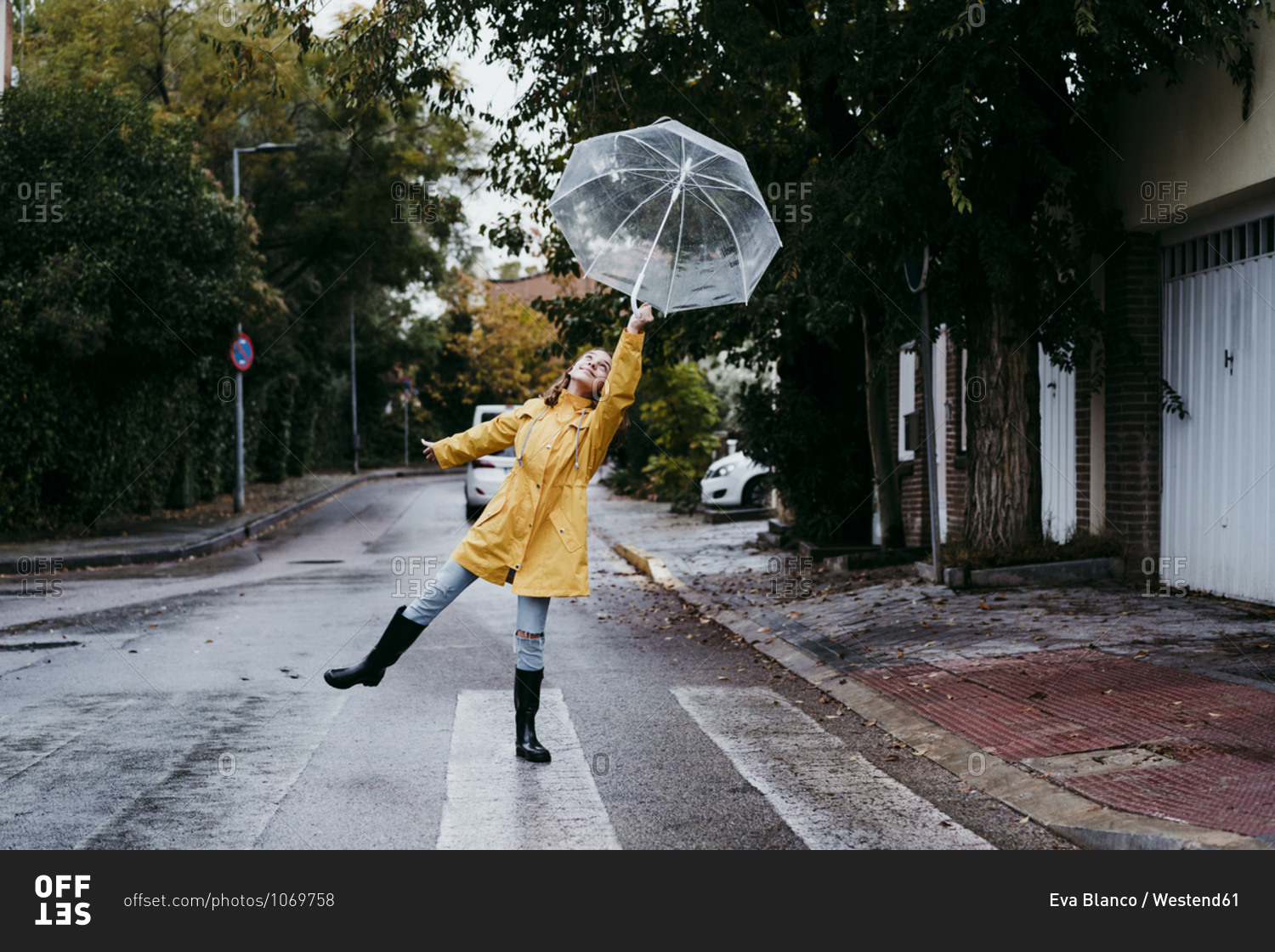 Girl wearing raincoat dancing with umbrella while standing on road in city
