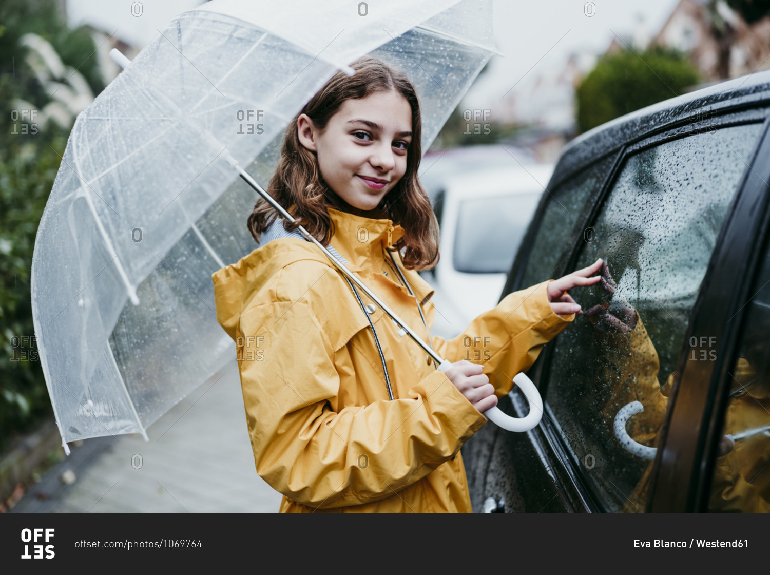 Smiling girl in raincoat holding umbrella while standing by car in city
