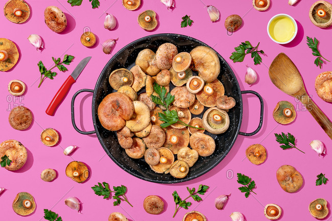 High angle view of mushrooms- parsley and garlic in cooking pan on pink background