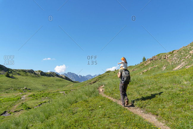 Father carrying daughter on shoulder while hiking in mountain during sunny day