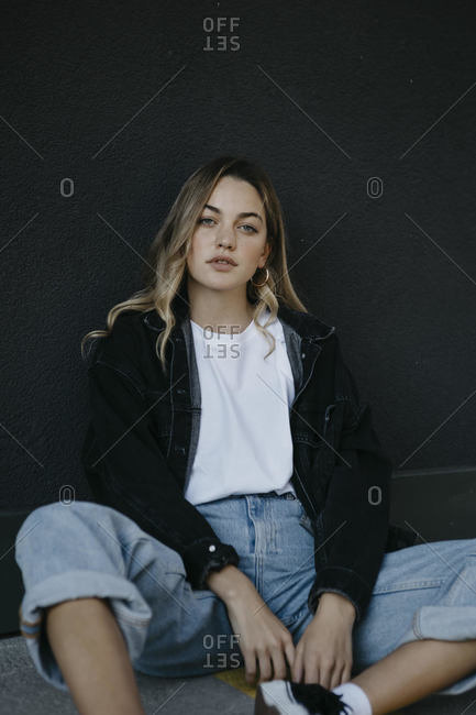 Contemplating young woman sitting on footpath against wall